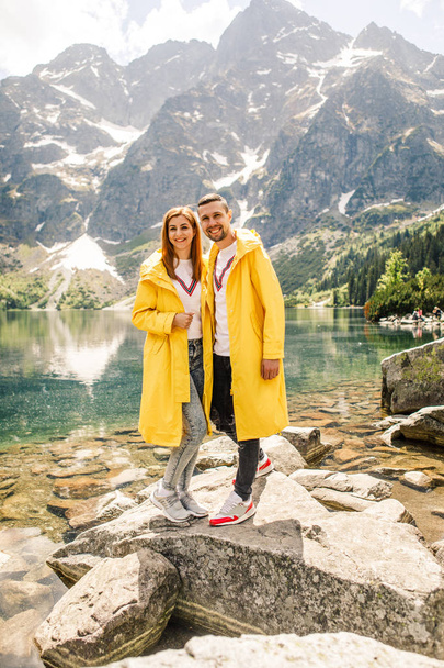 Young couple in yellow raincoats on walk inTatra Mountains near lake Morskie Oko, Poland - Foto, Imagen