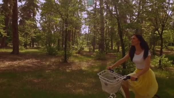 caucasian woman with long red hair enjoy active lifestyle. female riding on bike in park with green pines summer season lights of a sun - Séquence, vidéo
