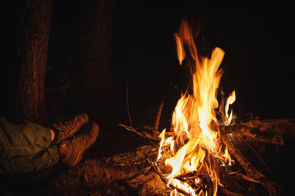 Night bonfire in tourist camp and legs of traveler outdoor. Tourism concept - Photo, Image