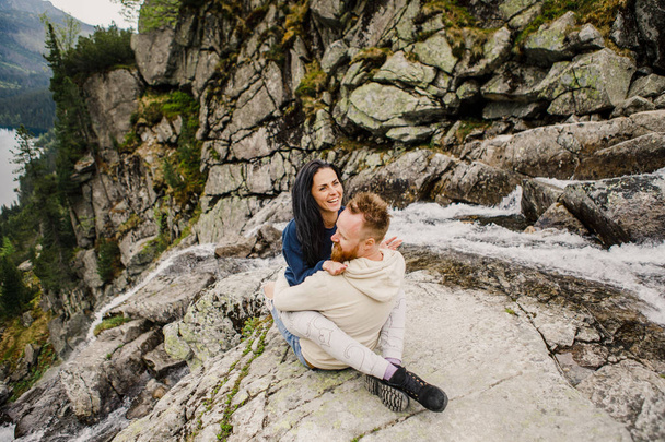 Young couple sitting at the edge of rock in norwegian fjord - Фото, изображение