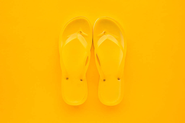 Top view of yellow flip flops pair on same color background with copy space. Beach sandals or slippers in minimalistic warm summer toned composition. - Фото, зображення