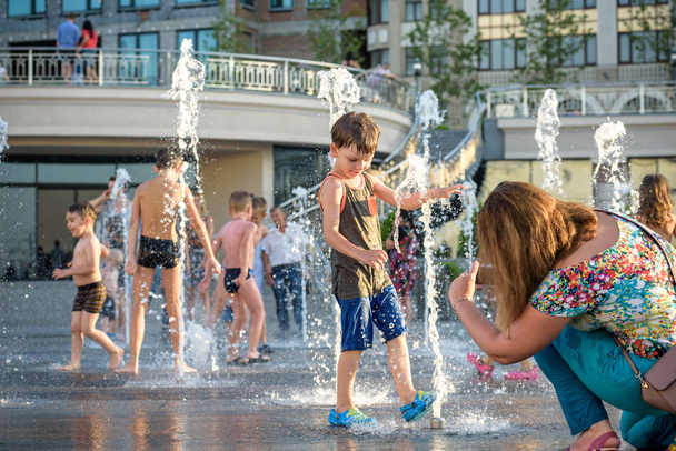 KYIV, UKRAINE AUGUST 13, 2017: Happy kids have fun playing in city water fountain on hot summer day. Parents with their children. Active family leisure, ecology concept. - Photo, image