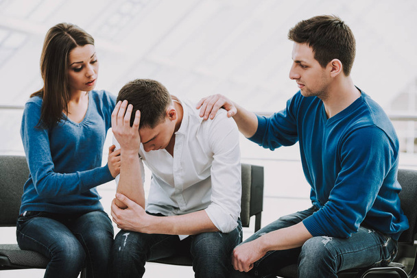 Feeling pain and depression. Depressed young man sitting at chair while two other people comforting his. - Foto, imagen