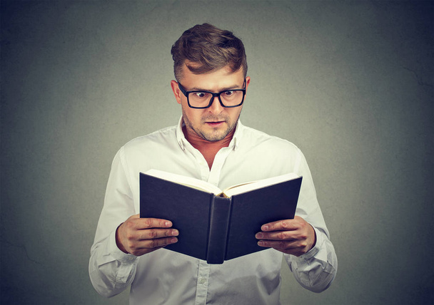 Man in glasses holding textbook and reading information with gasp looking super excited with news - Φωτογραφία, εικόνα