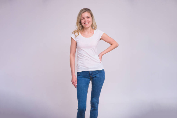 portrait of a beautiful blonde girl on a white background in different poses with different emotions. She is standing right in front of the camera smiling and looking happy - Φωτογραφία, εικόνα