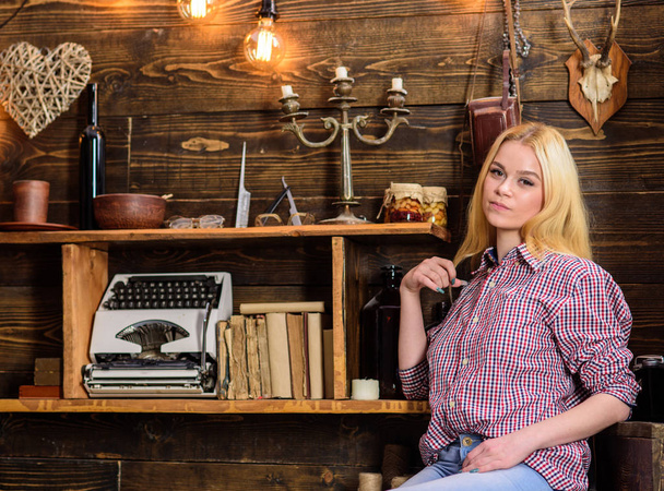 Girl sits and relaxing in house of gamekeeper. Girl in casual outfit sits in wooden vintage interior. Lady blonde on calm face in plaid clothes looks cute and casual. Vacation concept - Fotó, kép