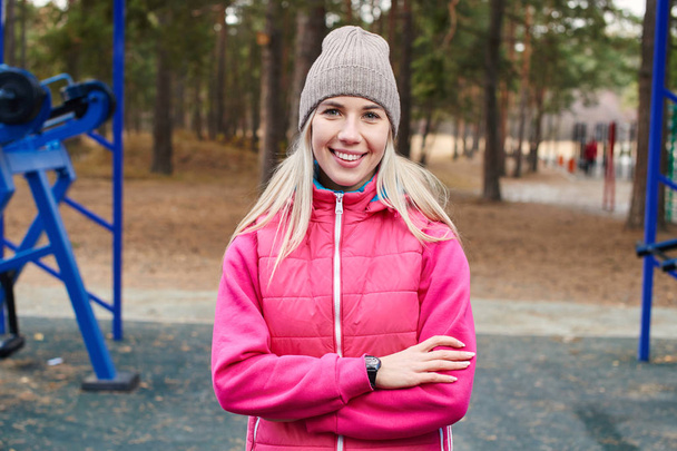 blonde woman athlete in jacket and hat with crossed arms standing outdoor  - Foto, Bild