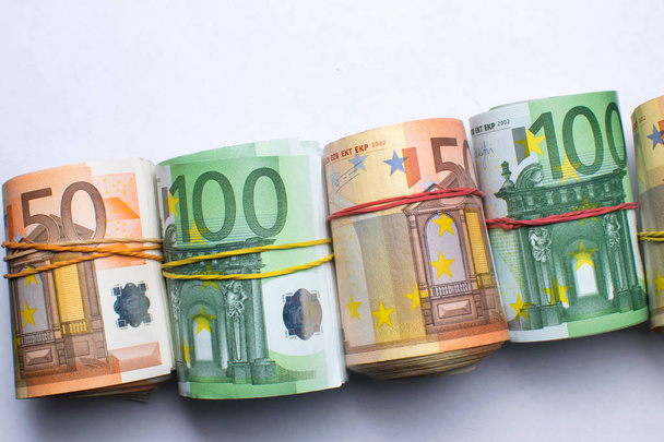 Hengerelt több ezer euro-bankjegyek gumik háttérrel. Euro valuta, hengerelt bankjegy fehér háttér. - Fotó, kép