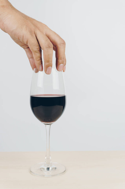 χέρι βάζει ένα ποτήρι κόκκινο κρασί πάνω στο ξύλινο τραπέζι - Φωτογραφία, εικόνα