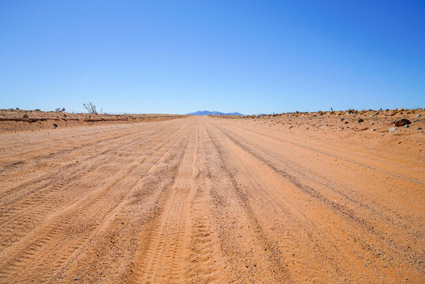 Renkaanjäljet pölyisellä punaisella hiekkatiellä ulottuvat kauas Namibian maiseman läpi
. - Valokuva, kuva