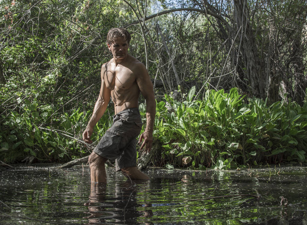 Muscular shirtless adventure man hiking through lush swamp environment - Photo, image