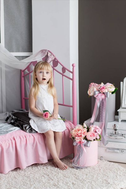 Little blonde girl in her room decorated with flowers. Portrait of a princess in a pink interior. Surprised baby face - Foto, Imagen