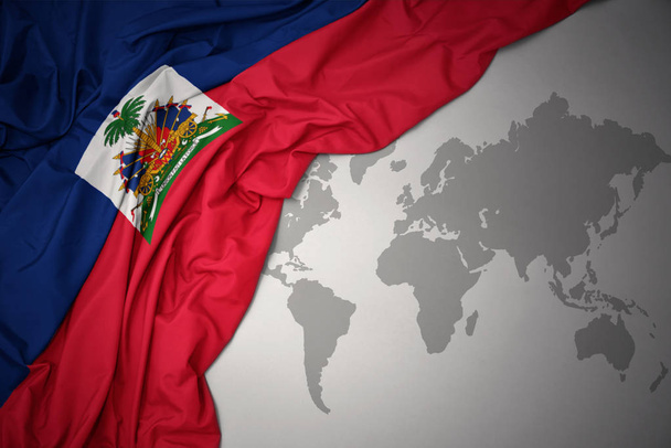 wuivende kleurrijke nationale vlag van Haïti op een grijze wereld kaart achtergrond. - Foto, afbeelding