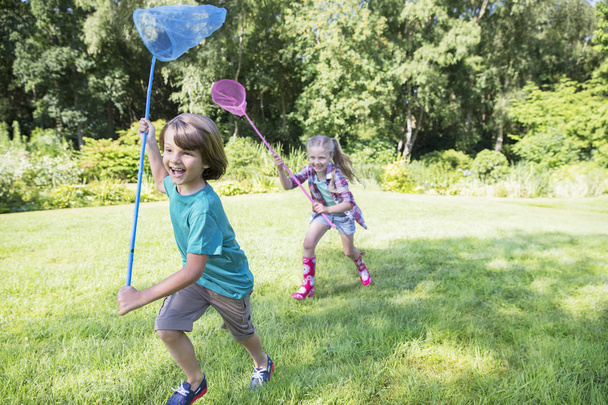 Niño y niña corriendo con redes de mariposa en la hierba
 - Foto, Imagen