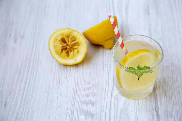 Лимонадний напій у склянці зі свіжим лимоном та м'ятою на білому дерев'яному фоні, вид збоку
.  - Фото, зображення