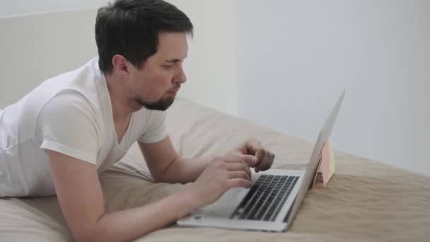 Mies painaa näppäimiä kannettavan näppäimistöllä, makaa sängyssä makuuhuoneessa
 - Materiaali, video