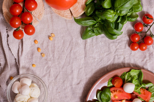 Caesar salad with white mozzarella cheese and cherry tomatoes, fresh basilon a gray linen napkin. wooden table, copy space. - Foto, Imagem