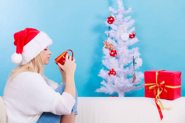 Relaxation during Christmas time concept. Woman in Santa hat holding holiday mug and drinking hot drink, coffee or tea enjoying her leisure time for relax. - Φωτογραφία, εικόνα