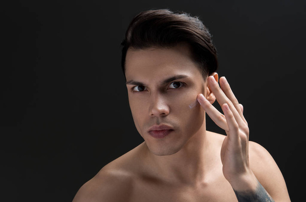 Gorgeous young guy is applying anti-aging cream on his skin - Foto, Imagen