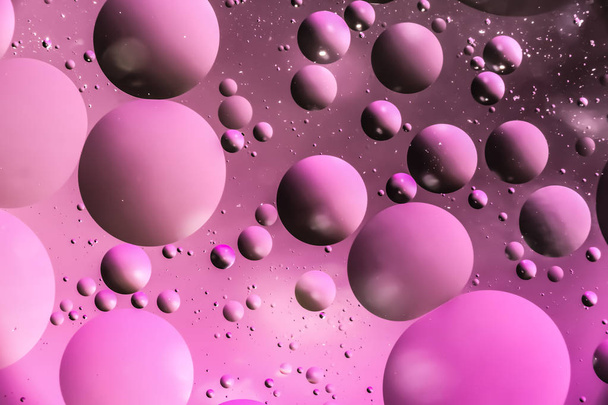 drops of oil in the form of circles and ovals chaotically located on the water surface, dark macro pink abstract background - Photo, Image
