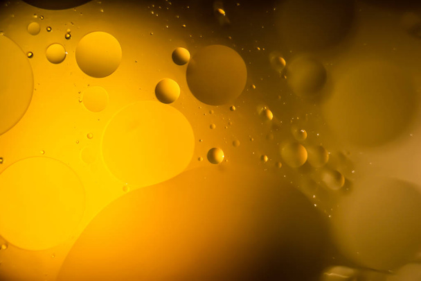 the interaction of water and oil, oil bubbles of various sizes on the water surface, yellow and black abstract macro background with soft defocusing - Fotó, kép