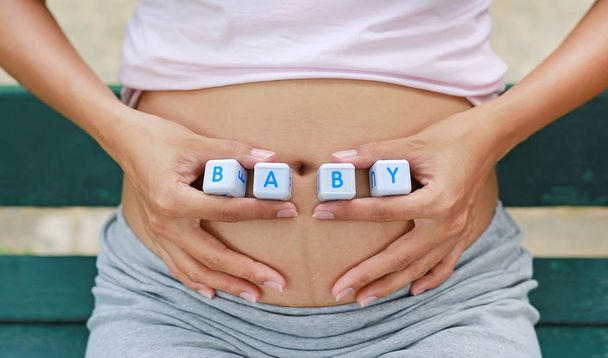 Close-up woman holding character cubic "BABY" at her belly. - Photo, image