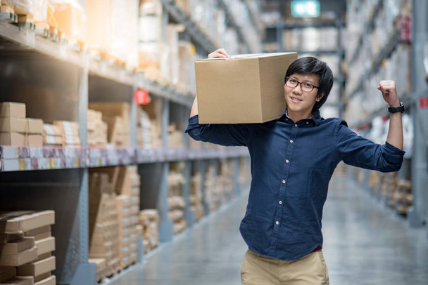 Mladá Asijská šťastný muž přepravní krabici mezi řadu poliček do skladu, skladování nebo práce vyskladnění a balení pojmy - Fotografie, Obrázek