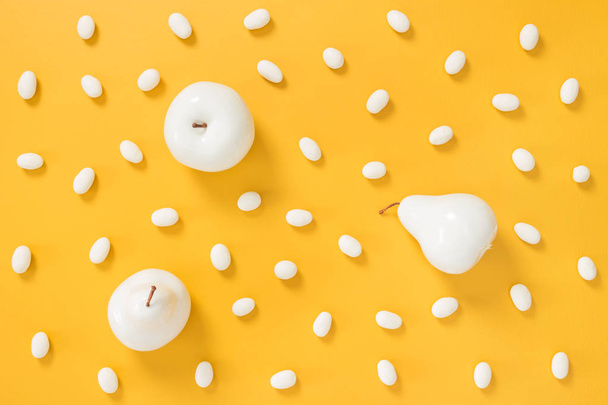 Caramelos de chocolate blanco y frutas pintadas sobre un vibrante fondo amarillo
. - Foto, imagen