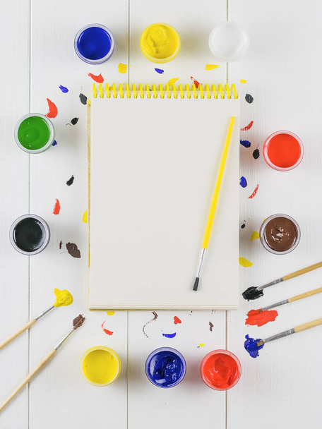 A drawing album with a brush and jars of paint on a white wooden table. Creative kit. Hobby and style. Flat lay. - Photo, Image