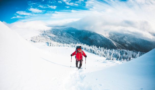 Un hombre con raquetas de nieve y bastones de trekking en las montañas. Viaje de invierno. Escalada de un escalador contra un hermoso cielo con nubes. Estilo de vida activo. Escalando la montaña a través de la nieve
. - Foto, Imagen