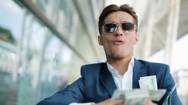 Young happy businessman scatter the dollars in the street. It is located near the office center, slow motion. Successful business or winning the lottery - Imágenes, Vídeo