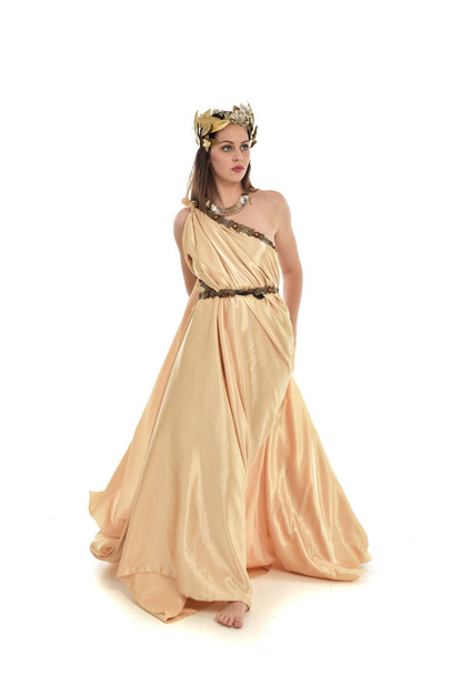 Ganzkörperporträt einer brünetten Frau im goldenen griechischen Gewand, die stehend posiert. isoliert auf weißem Studiohintergrund. - Foto, Bild