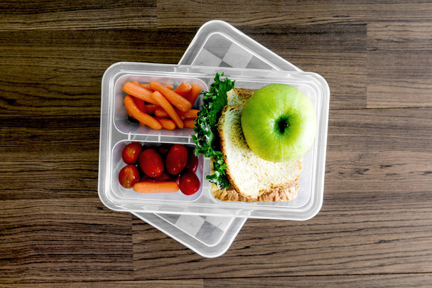 Lunch box with vegetables and slice of bread for a healthy school lunch on wooden table - Photo, Image