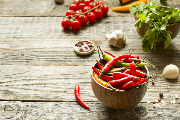 Chili pepper is spicy in a wooden bowl. Tomato parsley garlic on wooden rustic background. - Photo, image