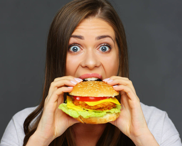 portrait of young woman biting big burger on gray wall background, fast food concept  - Valokuva, kuva