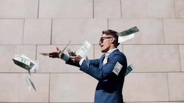 Young happy businessman scatter the dollars and funny dancing in the street. Money rain, falling dollars. It is located near the office center, slow motion. Successful business. Shot on Red Epic - Materiał filmowy, wideo