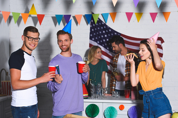 jonge mannen glimlachend in de camera terwijl bier drinken en feesten met vrienden - Foto, afbeelding