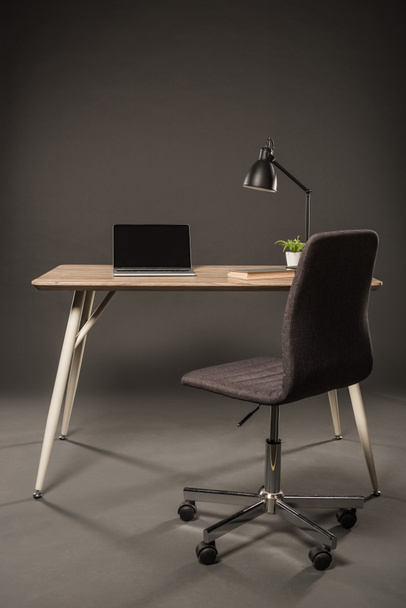 silla y mesa con lámpara, planta, libro y portátil con pantalla en blanco sobre fondo gris
  - Foto, Imagen