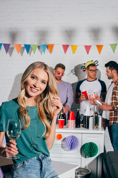 beautiful girl with wine glass smiling at camera while friends drinking behind - Valokuva, kuva