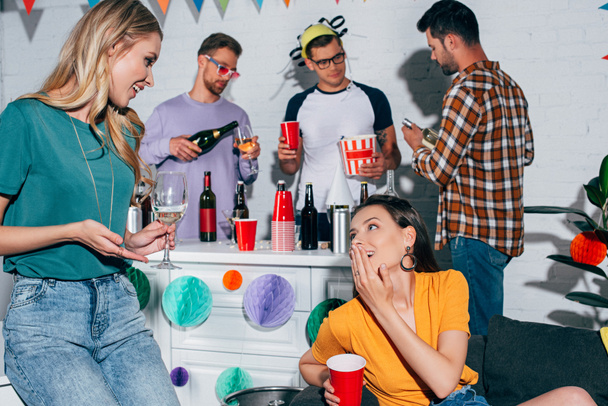 Улыбающиеся подруги пьют алкогольные напитки и разговаривают на домашней вечеринке
 - Фото, изображение