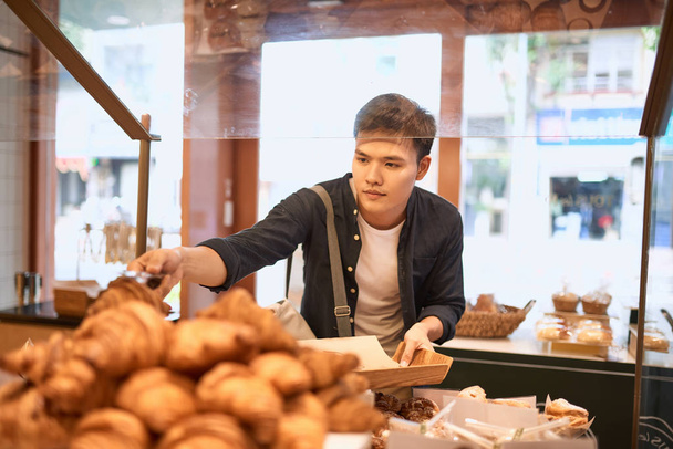 un hombre guapo con bandeja en la panadería comprando bollos
 - Foto, Imagen