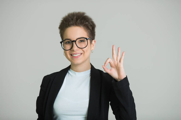 young beautiful girl with short hair on her head and with glasses with a short haircut on a gray background - Photo, image