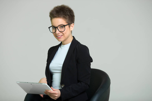 young beautiful girl with short hair on her head, in a suit and glasses with a tablet in her hands - Photo, image