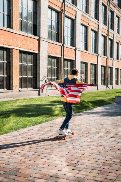 back view of man with american flag skating on longboard on street - Photo, Image