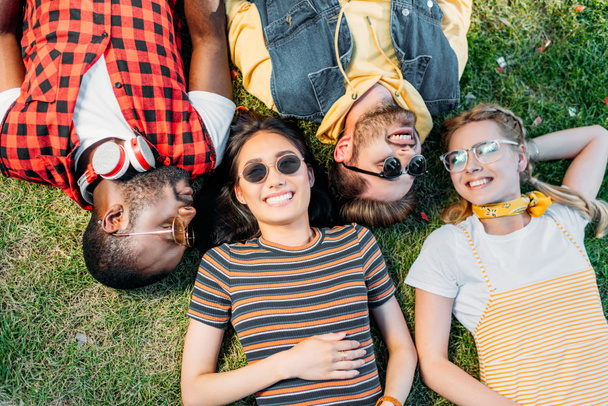 Blick von oben auf glückliche multiethnische Freunde, die gemeinsam auf grünem Rasen ruhen - Foto, Bild