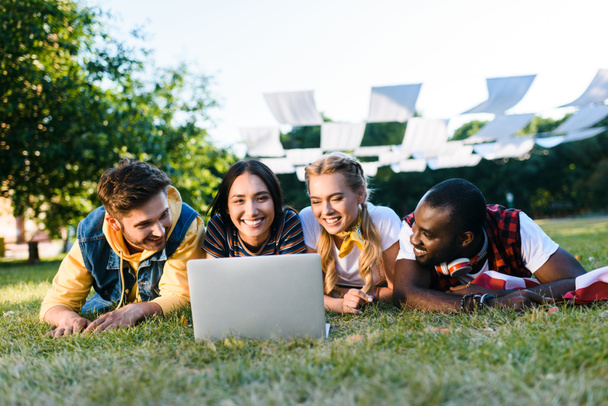 portrait of interracial young friends with laptop resting on green lawn in park - Foto, immagini