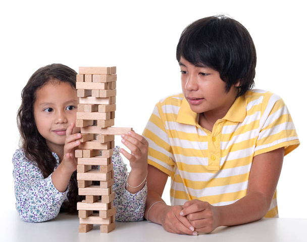 Τα παιδιά παίζουν και σωρός ένα πύργο από ξύλινες πέτρες ενάντια σε λευκό φόντο - Φωτογραφία, εικόνα