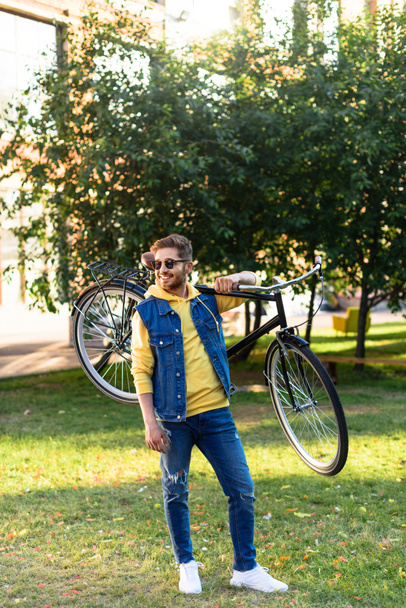 young cheerful man in sunglasses with retro bicycle in park - Fotoğraf, Görsel