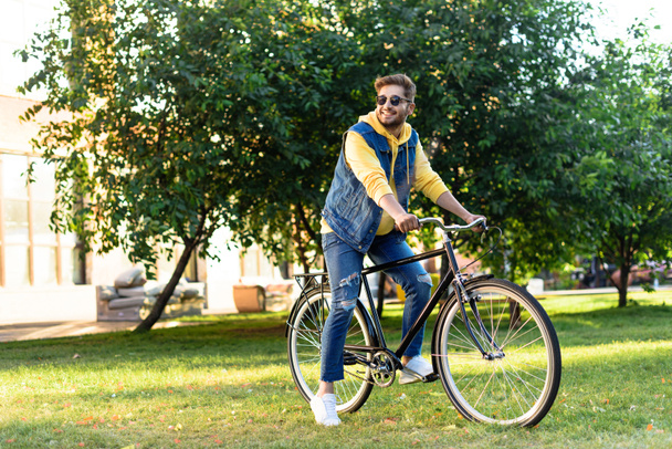 young smiling man in sunglasses riding retro bicycle in park - Fotografie, Obrázek