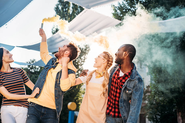 interracial cheerful young friends with colorful smoke bomb in park - Фото, зображення